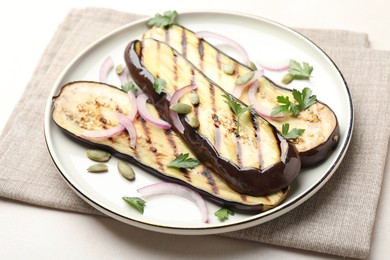 Photo of Slices of grilled eggplant, parsley, pumpkin seeds and onion on white table, closeup
