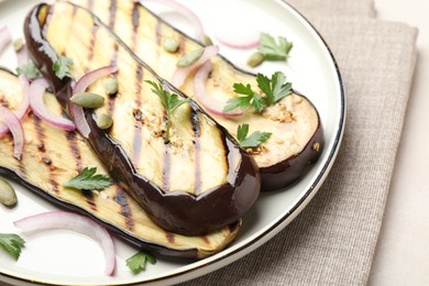 Photo of Slices of grilled eggplant, parsley, pumpkin seeds and onion on white table, closeup