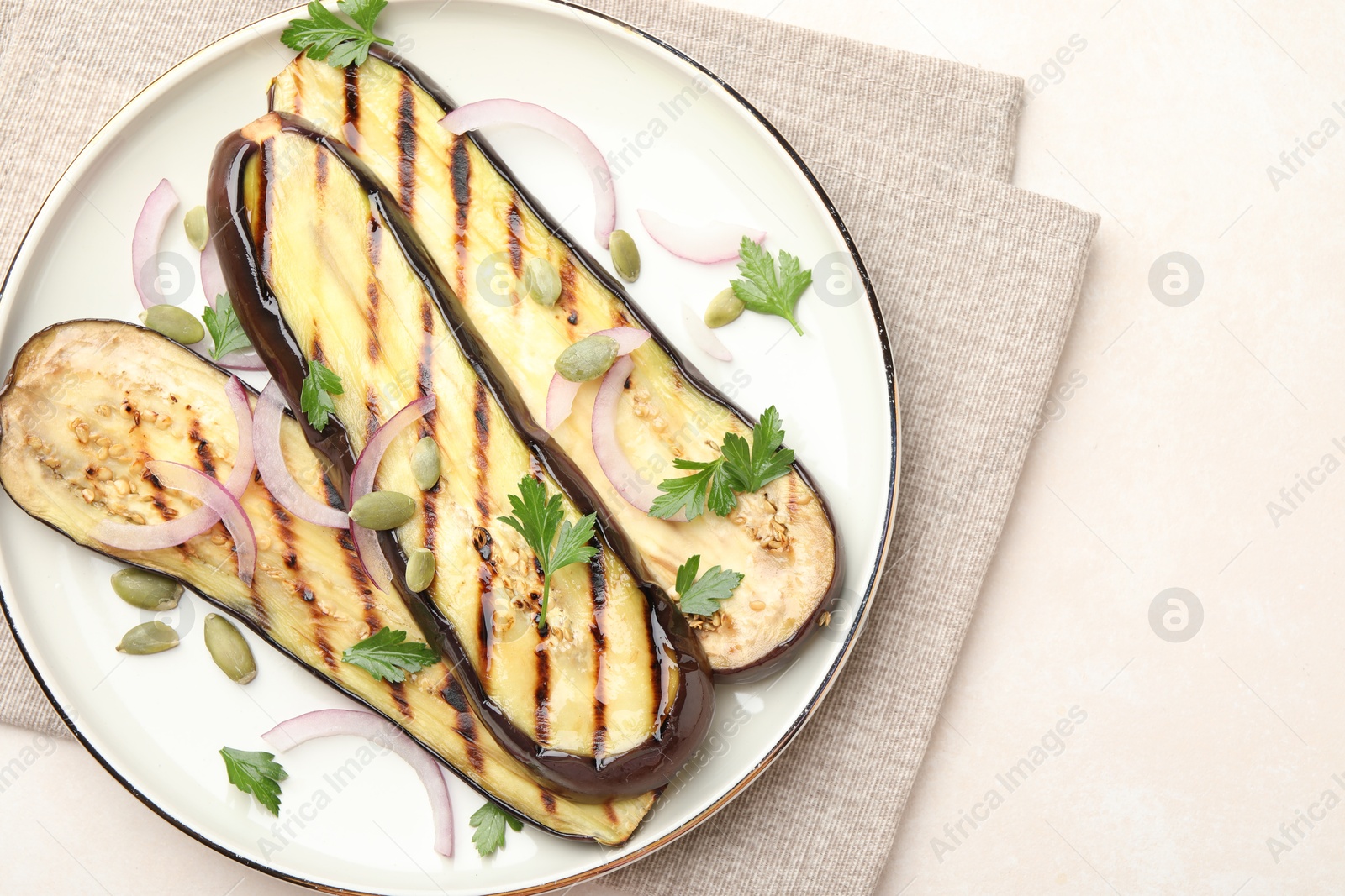 Slices of grilled eggplant, parsley, pumpkin seeds and onion on white table, top view. Space for text Photo of Slices of grilled eggplant, parsley, pumpkin seeds and onion on white table, top view. Space for text