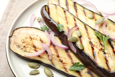 Photo of Slices of grilled eggplant, parsley, pumpkin seeds and onion on table, closeup