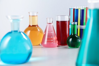 Photo of Different laboratory glassware with color liquids on light background, closeup