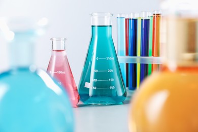 Photo of Different laboratory glassware with color liquids on light background, closeup