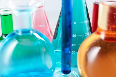 Photo of Different laboratory glassware with color liquids on light background, closeup