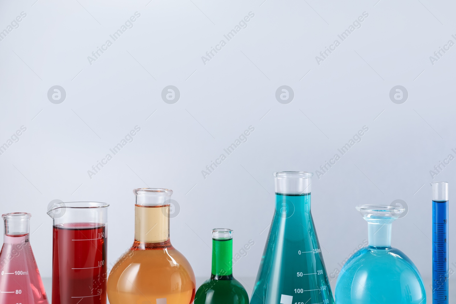 Different laboratory glassware with color liquids on light background. Space for text Photo of Different laboratory glassware with color liquids on light background. Space for text