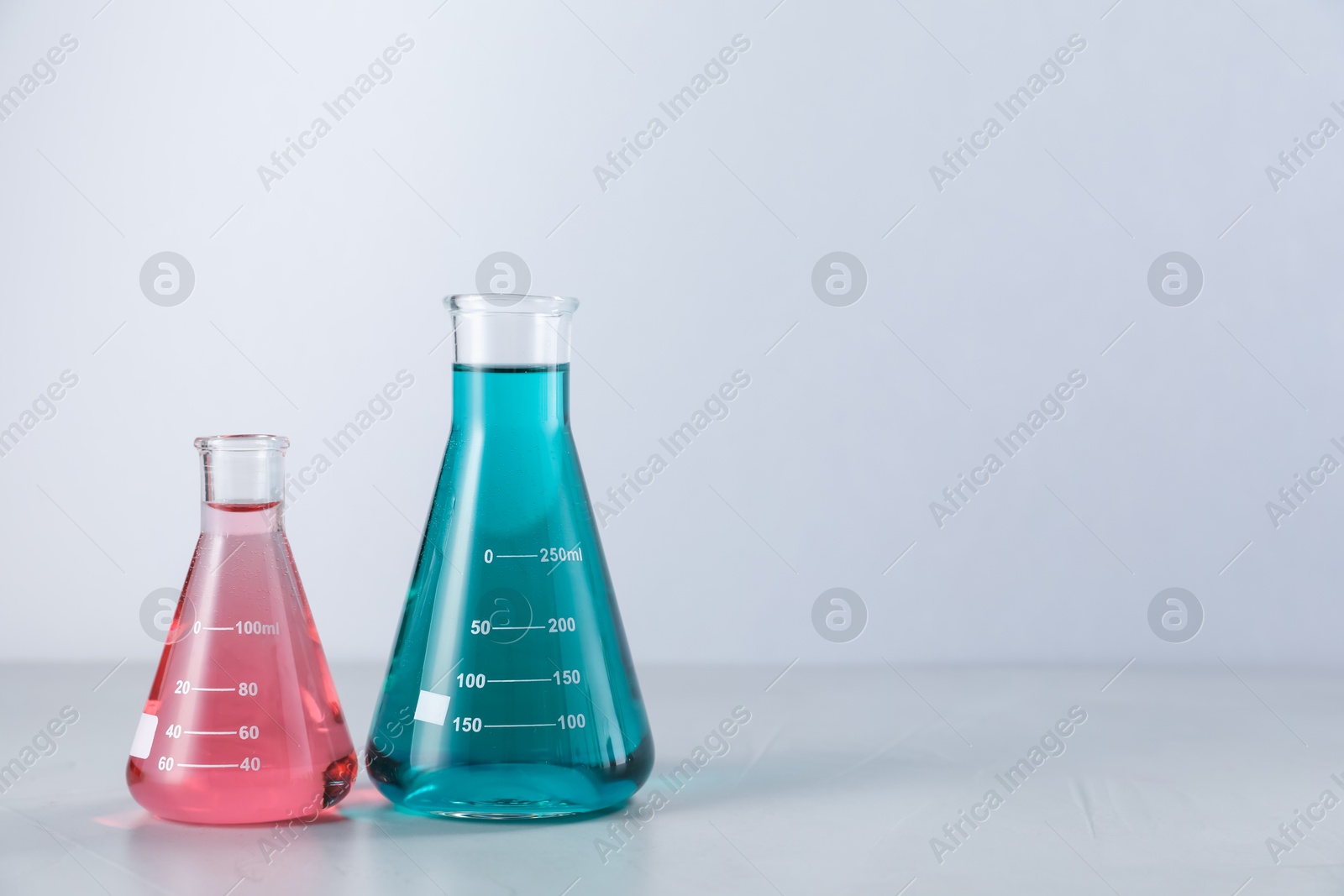Flasks with color liquids on light background. Space for text Photo of Flasks with color liquids on light background. Space for text
