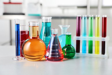 Photo of Different laboratory glassware with color liquids on light table indoors