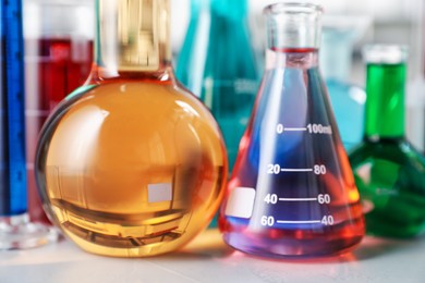 Photo of Different laboratory glassware with color liquids on light table, closeup