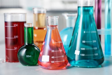 Photo of Different laboratory glassware with color liquids on light table indoors, closeup