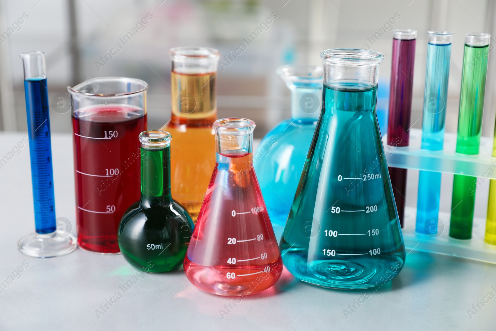 Different laboratory glassware with color liquids on light table indoors, closeup Photo of Different laboratory glassware with color liquids on light table indoors, closeup