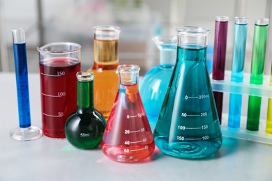 Photo of Different laboratory glassware with color liquids on light table indoors, closeup