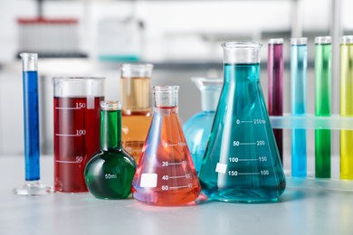 Photo of Different laboratory glassware with color liquids on light table indoors