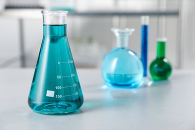Photo of Different laboratory glassware with color liquids on light table indoors, selective focus