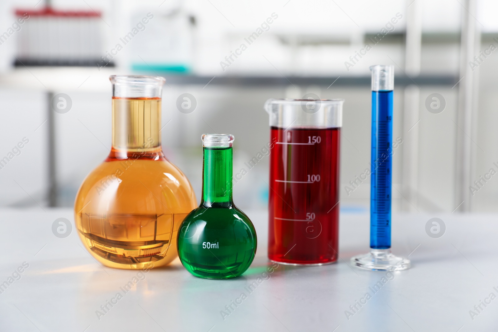 Different laboratory glassware with color liquids on light table indoors Photo of Different laboratory glassware with color liquids on light table indoors