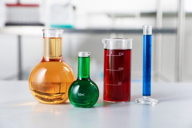 Photo of Different laboratory glassware with color liquids on light table indoors