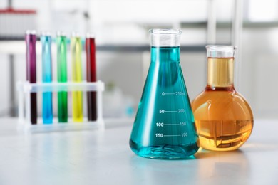 Photo of Different laboratory glassware with color liquids on light table indoors, selective focus