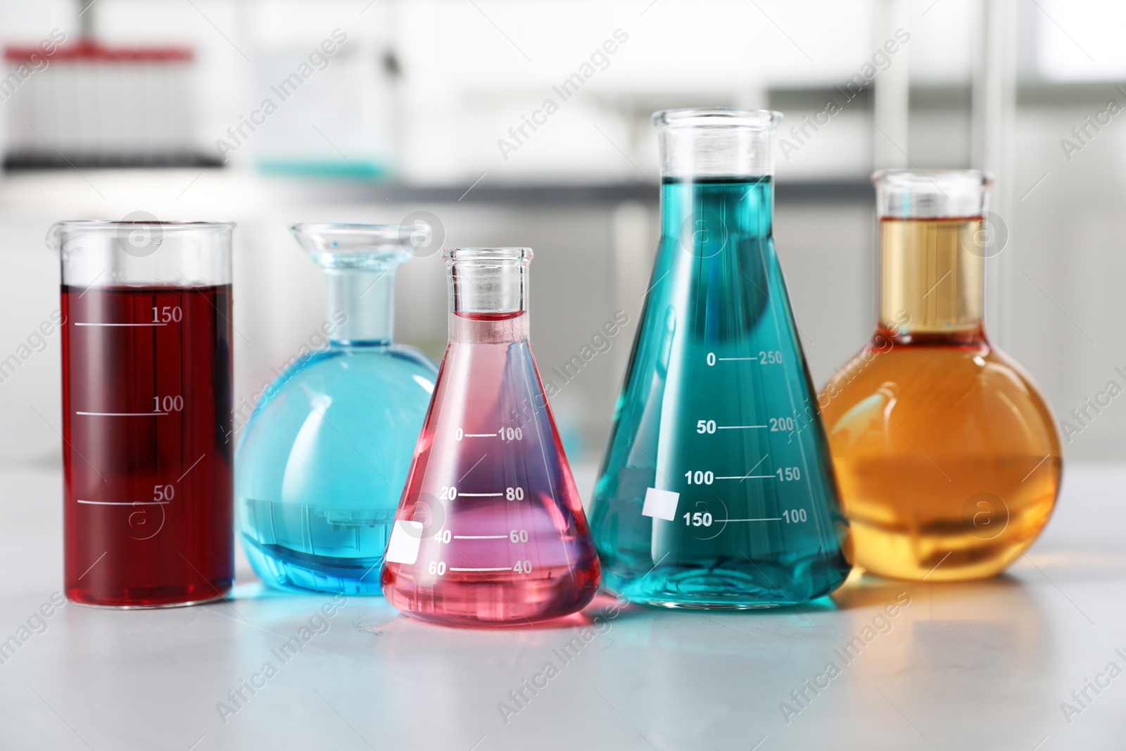 Different laboratory glassware with color liquids on light table indoors Photo of Different laboratory glassware with color liquids on light table indoors