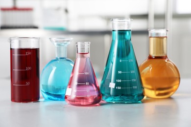 Photo of Different laboratory glassware with color liquids on light table indoors