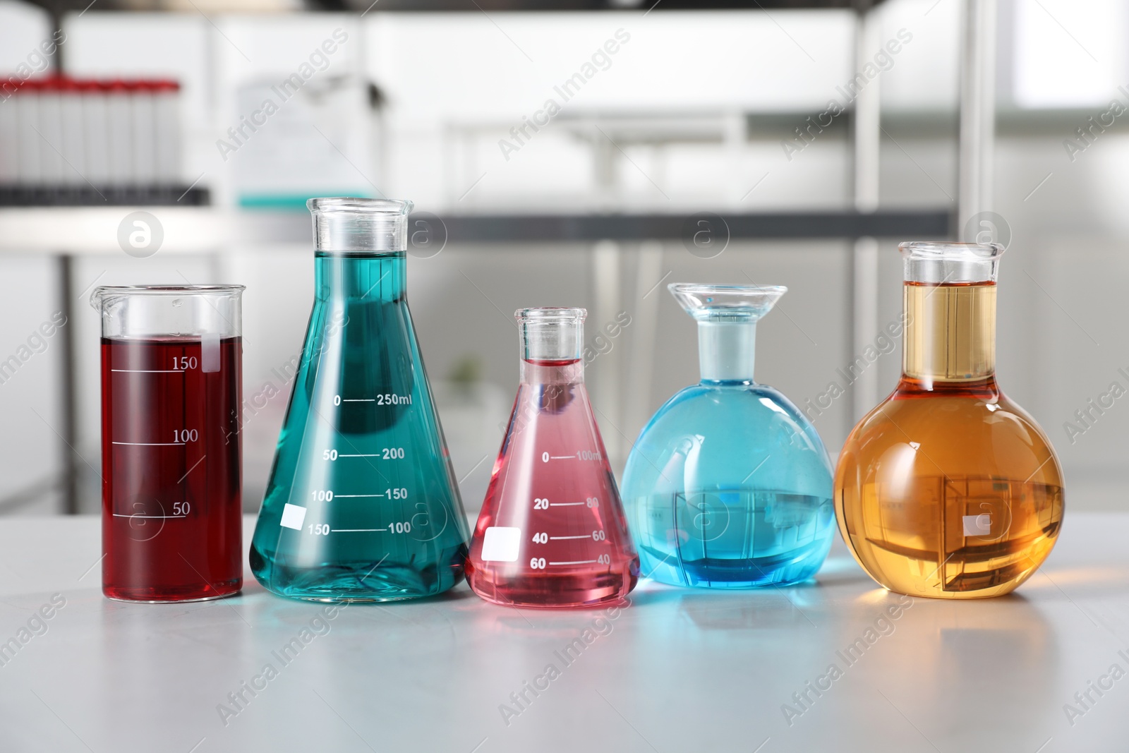 Different laboratory glassware with color liquids on light table indoors Photo of Different laboratory glassware with color liquids on light table indoors