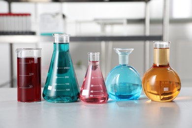 Photo of Different laboratory glassware with color liquids on light table indoors