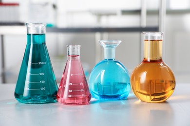Photo of Different laboratory glassware with color liquids on light table indoors