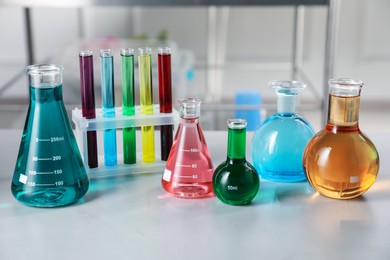 Photo of Different laboratory glassware with color liquids on light table indoors