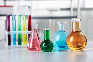 Photo of Different laboratory glassware with color liquids on light table indoors