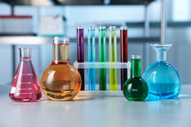 Photo of Different laboratory glassware with color liquids on light table indoors