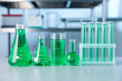 Photo of Different laboratory glassware with green liquid on light table indoors