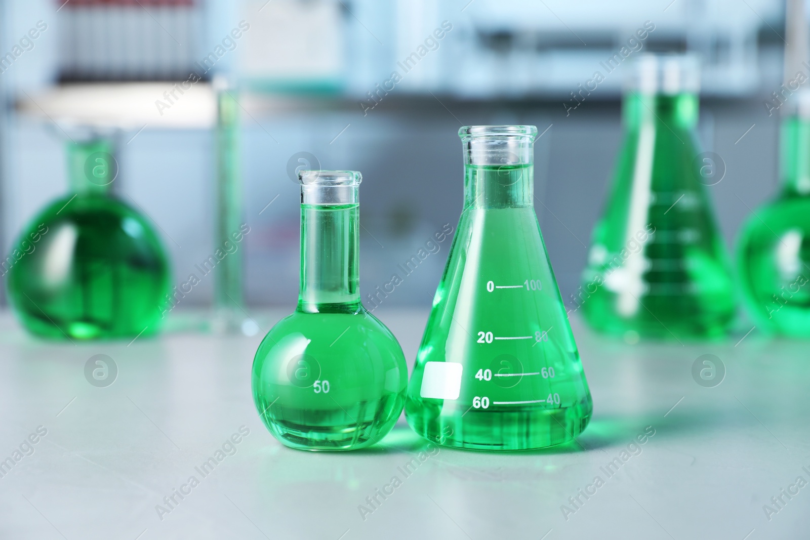 Photo of Different laboratory glassware with green liquid on light table indoors, selective focus
