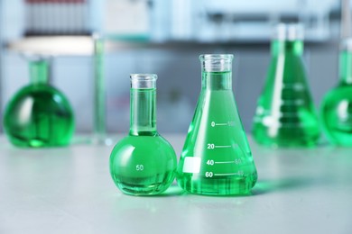Photo of Different laboratory glassware with green liquid on light table indoors, selective focus