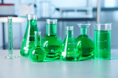 Photo of Different laboratory glassware with green liquid on light table indoors
