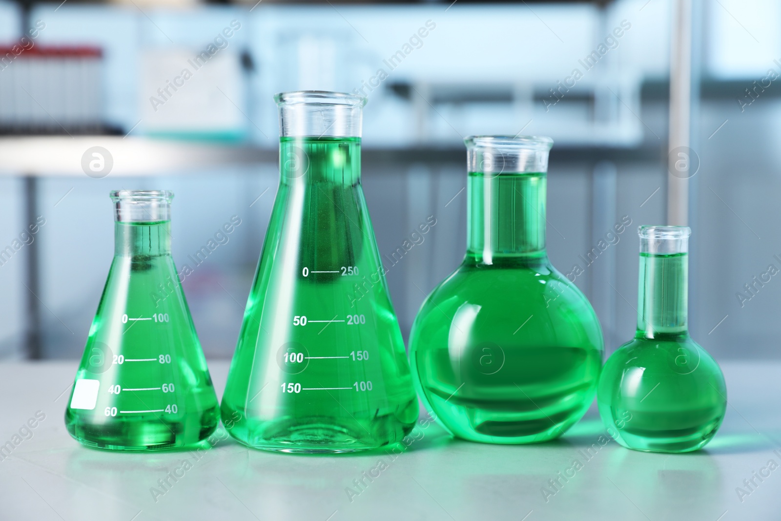 Photo of Different laboratory glassware with green liquid on light table indoors