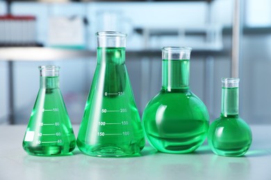 Photo of Different laboratory glassware with green liquid on light table indoors