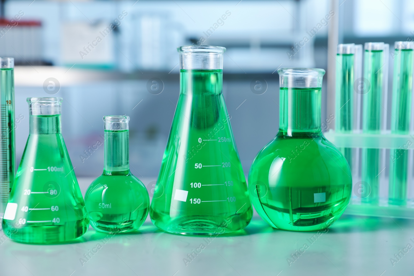Photo of Different laboratory glassware with green liquid on light table indoors