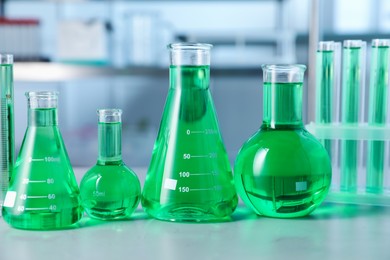 Photo of Different laboratory glassware with green liquid on light table indoors