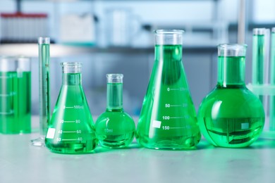 Photo of Different laboratory glassware with green liquid on light table indoors
