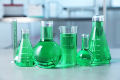 Photo of Different laboratory glassware with green liquid on light table indoors