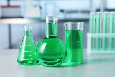 Photo of Different laboratory glassware with green liquid on light table indoors, selective focus