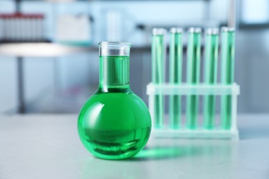 Photo of Different laboratory glassware with green liquid on light table indoors, selective focus
