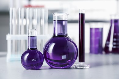 Photo of Different laboratory glassware with purple liquid on light table indoors, selective focus
