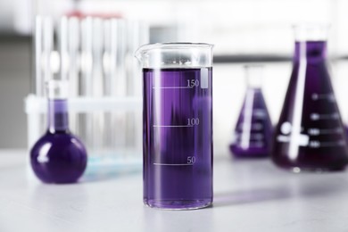 Photo of Different laboratory glassware with purple liquid on light table indoors, selective focus