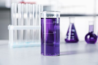 Photo of Different laboratory glassware with purple liquid on light table indoors, selective focus