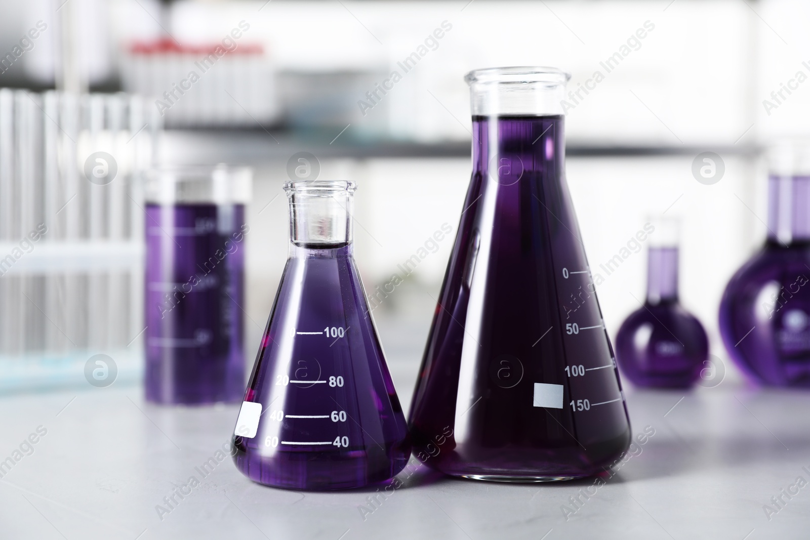 Photo of Different laboratory glassware with purple liquid on light table indoors, selective focus