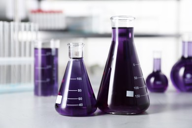 Photo of Different laboratory glassware with purple liquid on light table indoors, selective focus