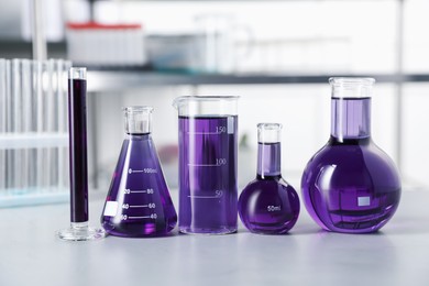Photo of Different laboratory glassware with purple liquid on light table indoors