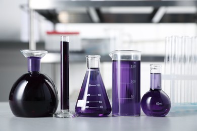 Photo of Different laboratory glassware with purple liquid on light table indoors