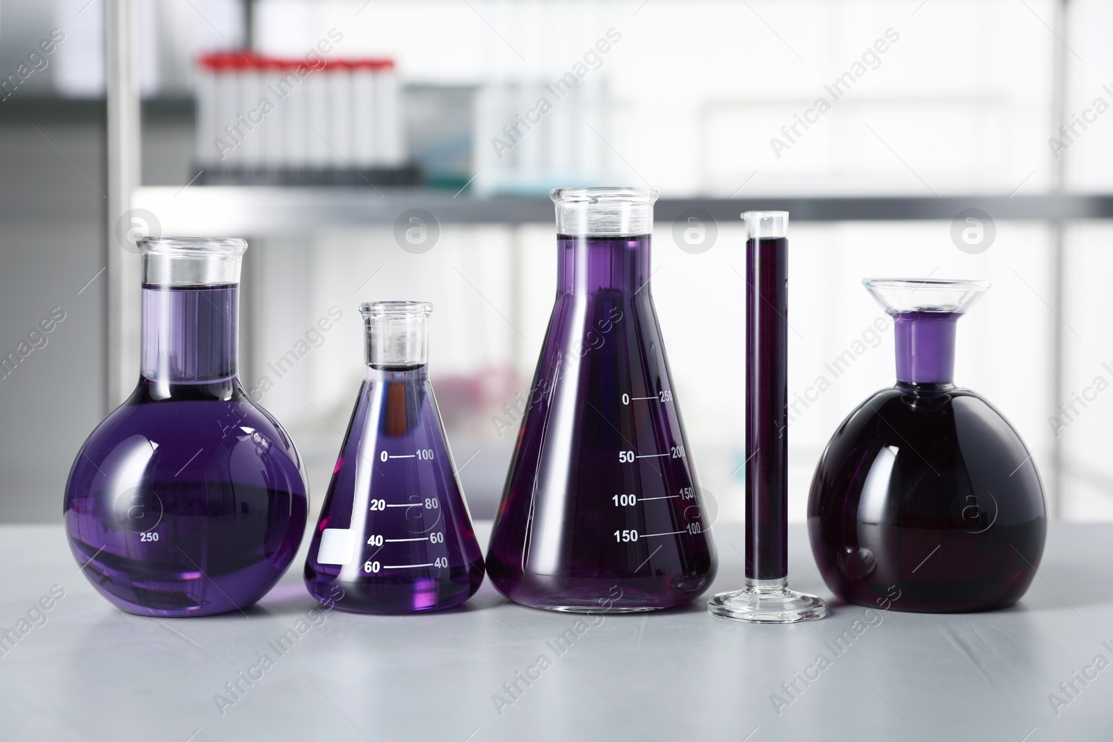 Photo of Different laboratory glassware with purple liquid on light table indoors