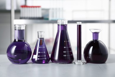Photo of Different laboratory glassware with purple liquid on light table indoors