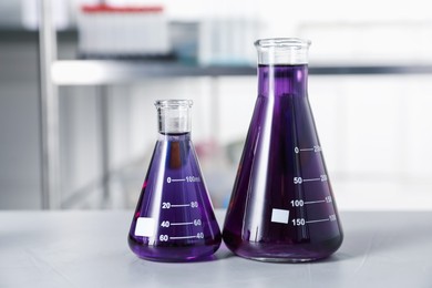 Photo of Flasks with purple liquid on light table indoors