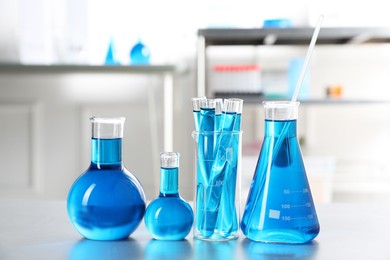 Photo of Different laboratory glassware with light blue liquid on table indoors